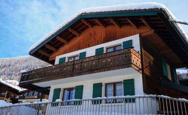 Chalet exterior with carved wooden balcony and green shutters