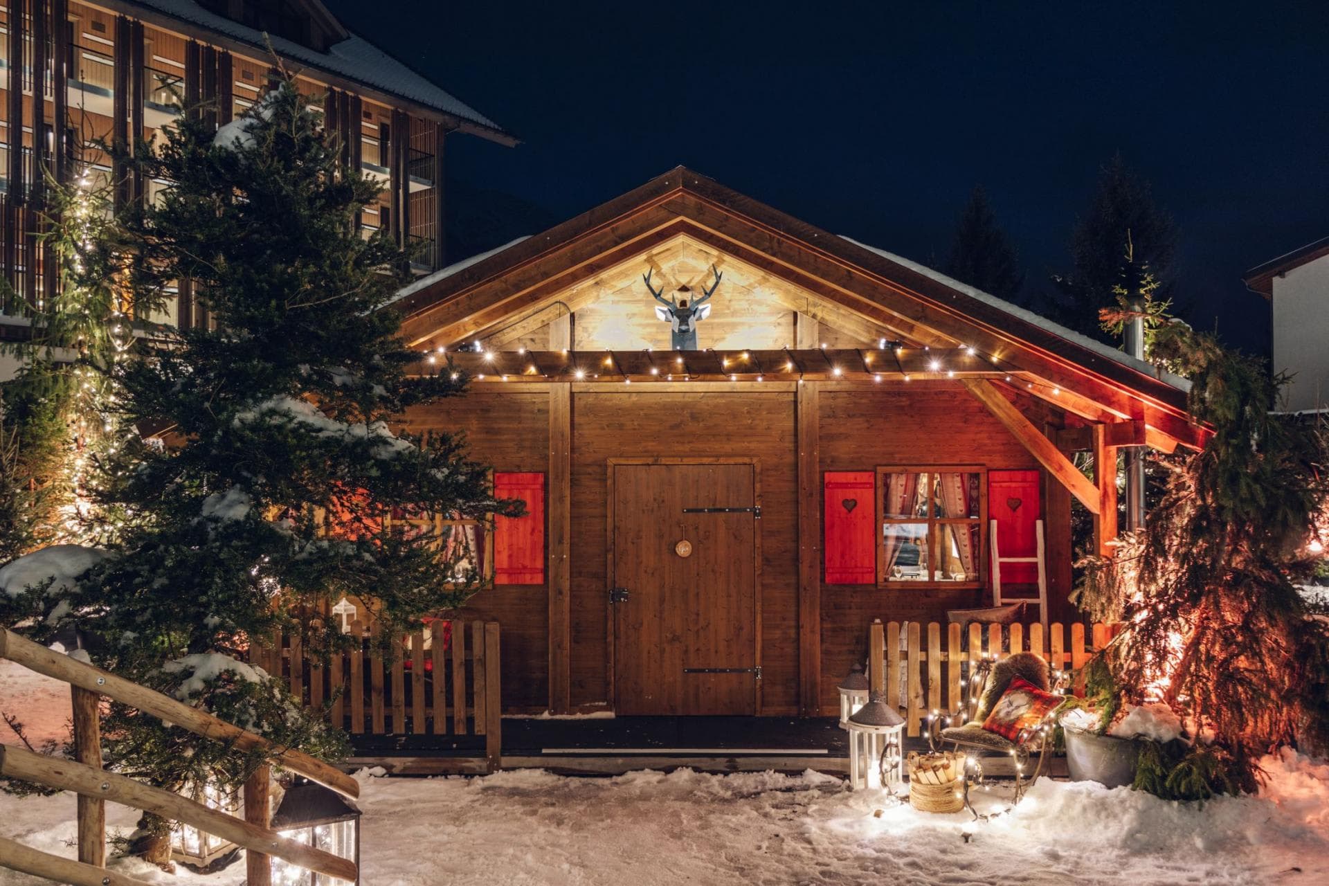 Cabin entrance with holiday lighting, wood fencing, and private snow-covered patio