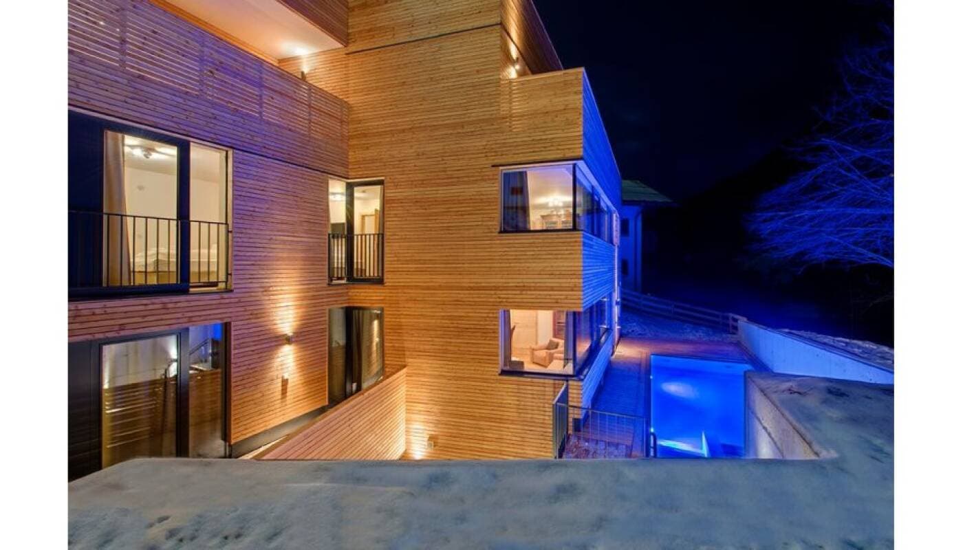 Modern home exterior with illuminated brick facade and heated infinity pool at night