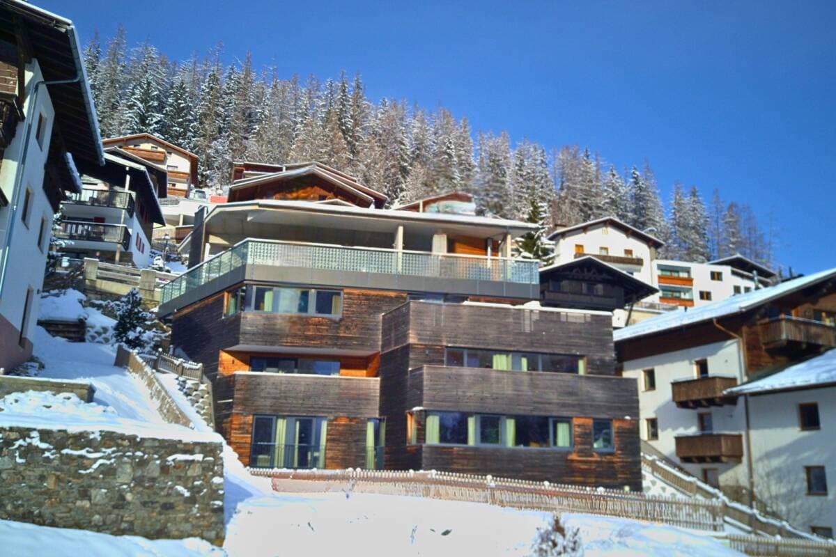 Modern chalet exterior with dark wood siding, multiple levels, and snow-covered alpine setting