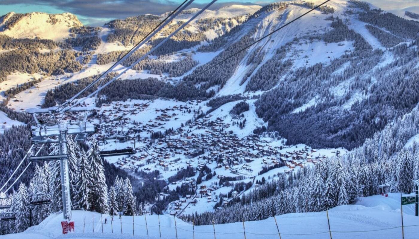 Ski resort village and slopes viewed from gondola; tree-lined valley with lift access