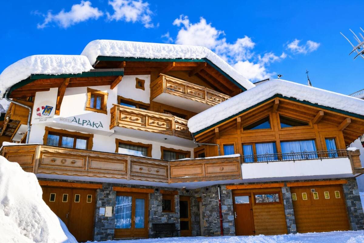 Alpine chalet exterior with snow-capped roof, wooden balconies, and heated garage bays