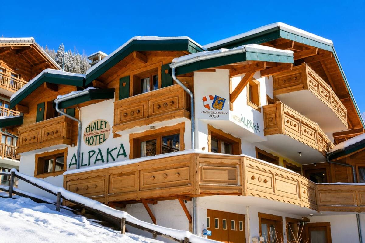 Chalet Alpaka exterior: carved wood balconies, green roof trim, snow setting