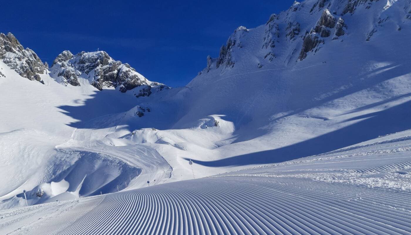Groomed ski run with corduroy texture; steep terrain visible above