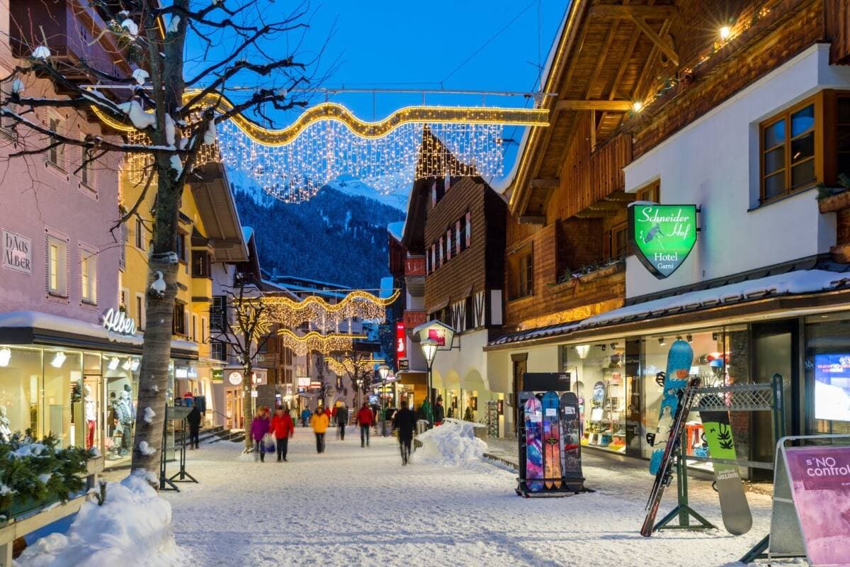 Village pedestrian street with holiday lights and mountain backdrop at dusk